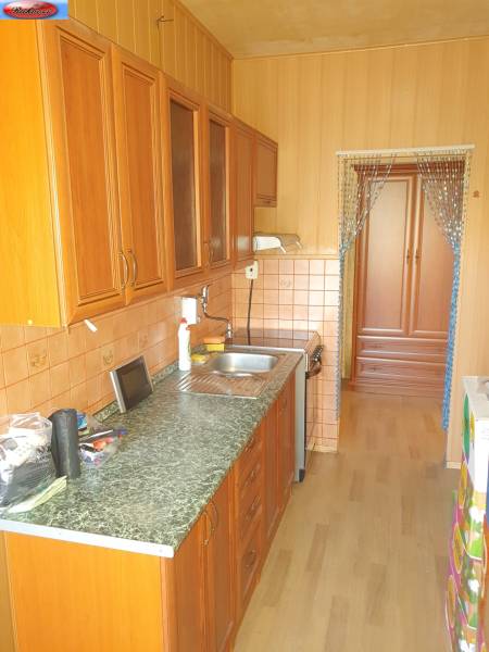 A kitchen in a 2-room apartment with wooden cabinets and tiled backsplash.