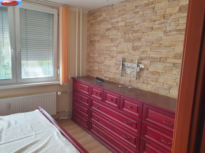 Bedroom in a 2-room apartment with stone wallpaper and wooden dressers.