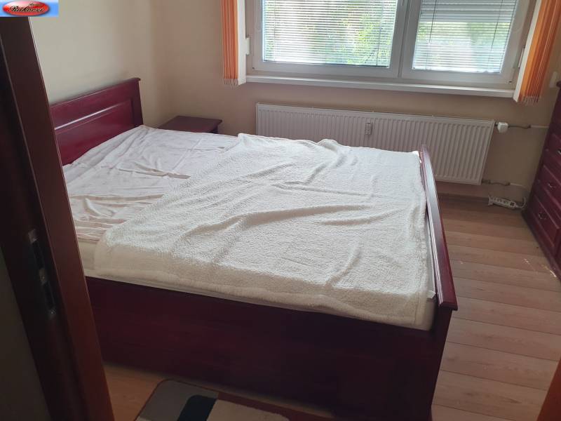 A bedroom in a two-room apartment with light wooden furniture and a window with blinds.