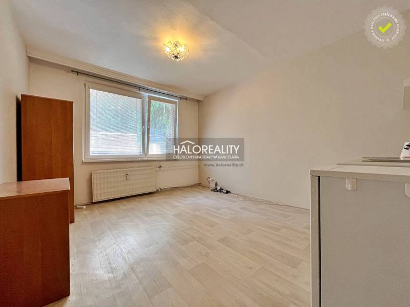 A studio apartment with a large window, light flooring, and simple furnishings.