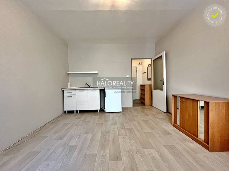 Studio apartment with a white kitchen unit, wooden furniture, and laminate flooring.