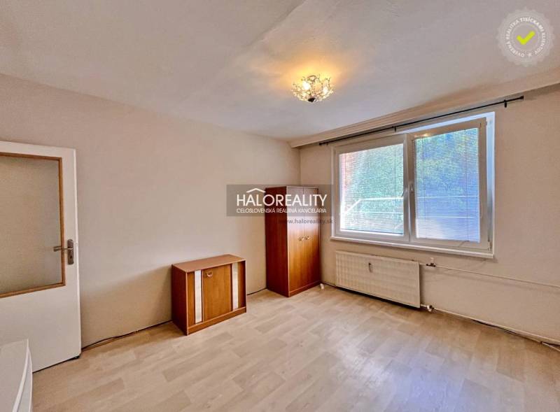 A studio apartment with wooden furniture and a large window, offering pleasant daylight.