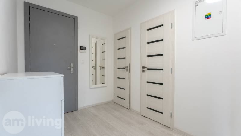 Entrance hallway in a 3-room apartment with a mirror, white furniture, and light-colored doors.