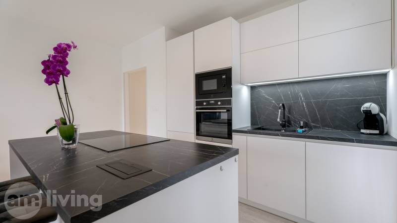 A kitchen in a 3-room apartment with white cabinets, a black countertop, and an orchid.
