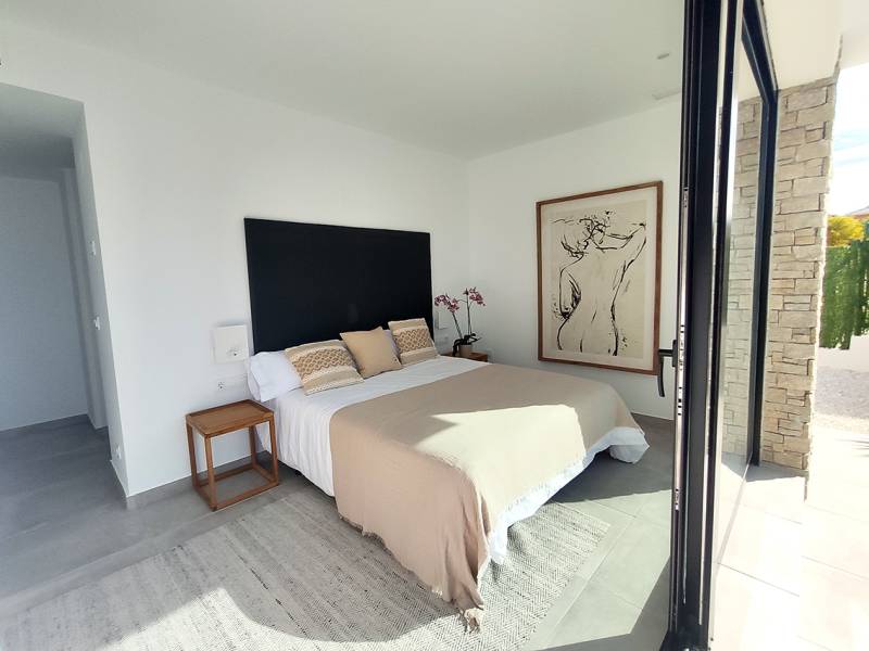 A bright bedroom in a villa with a bed, a painting on the wall, and a view outside.