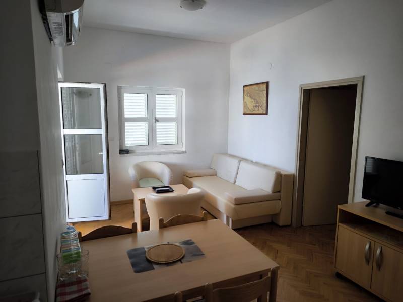 A clear one-room apartment with wooden flooring, a table, a television, and a sofa.