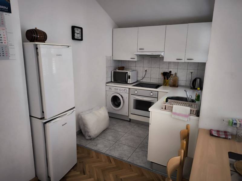 A kitchen in a studio apartment with white cabinets, appliances, and a wooden table.