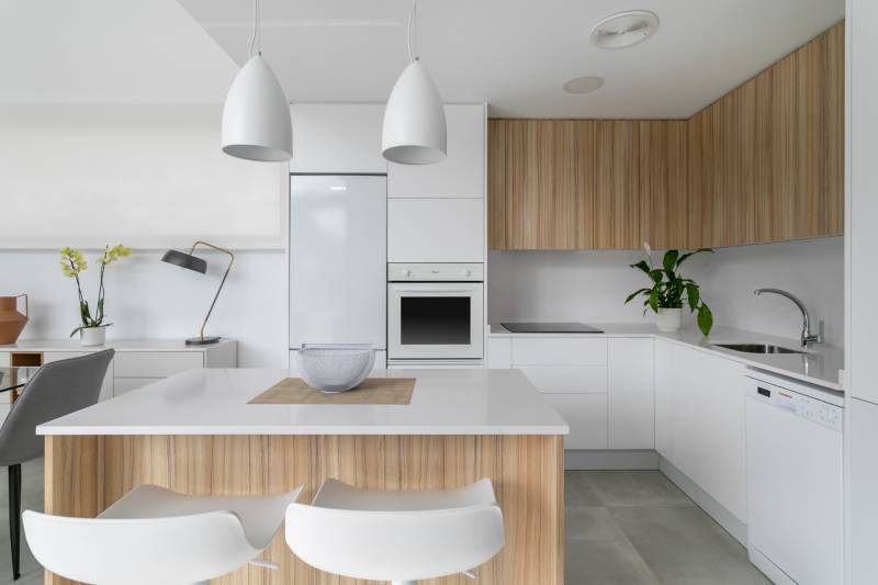 A kitchen in a villa with white and wooden cabinets, illuminated by modern lamps.
