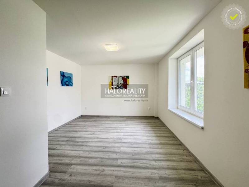 A spacious room with wooden flooring, white walls, and a large window in a family house.