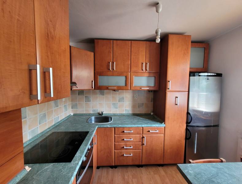 A kitchen in a studio apartment with wooden cabinets, a stainless steel sink, and an electric stove.