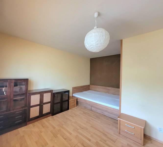 A simple room with a bed, cabinets, and wooden flooring in a studio apartment.
