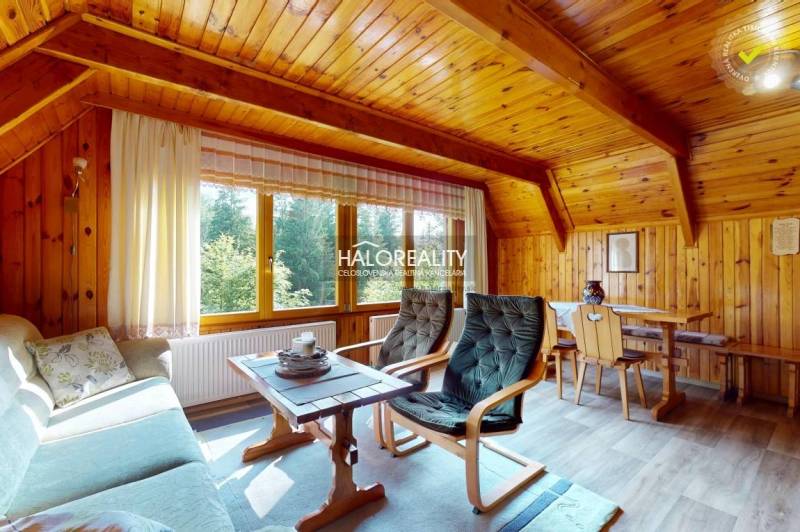 A wooden interior of a cabin with comfortable seating and a view of nature through a large window.