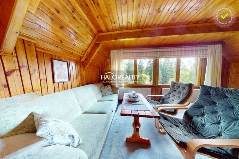 Wooden living room in a cabin with a sofa, armchairs, and a view of the forest.