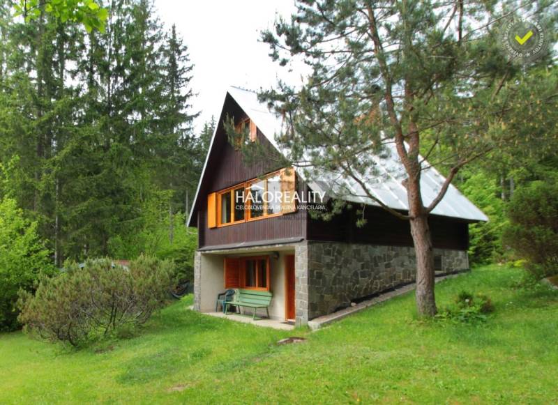 A cottage in the outskirts of Dolná Lehota surrounded by dense coniferous trees and a green lawn.