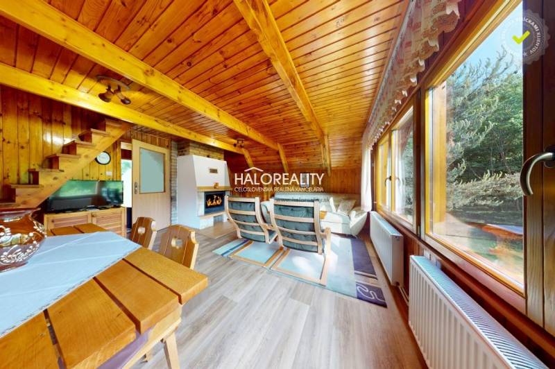 Wooden interior of a cabin with a fireplace, sofa, and view of the forest.