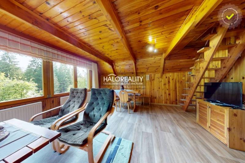 Wooden interior of a cabin with armchairs, a table, and a staircase in a mountain setting.