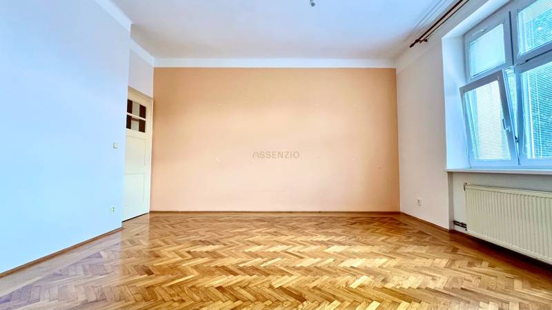 An empty room with a parquet floor and a large window in a two-room apartment.