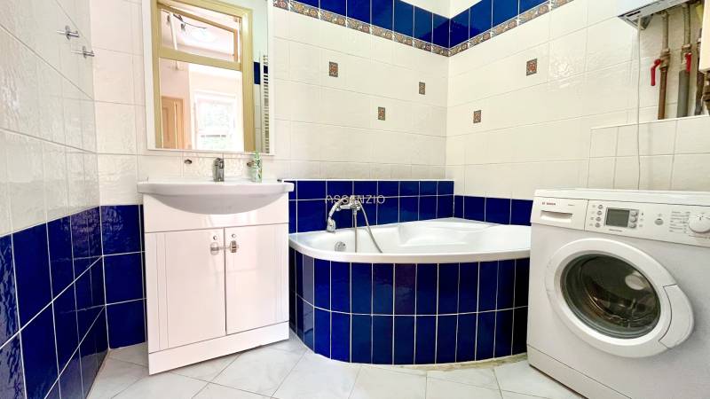 A bathroom in a 2-room apartment with a bathtub, sink, and washing machine, tiled with blue tiles.