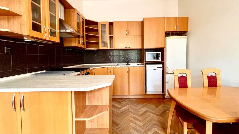 A kitchen in a 2-room apartment with wooden cabinets, a dining table, and parquet flooring.