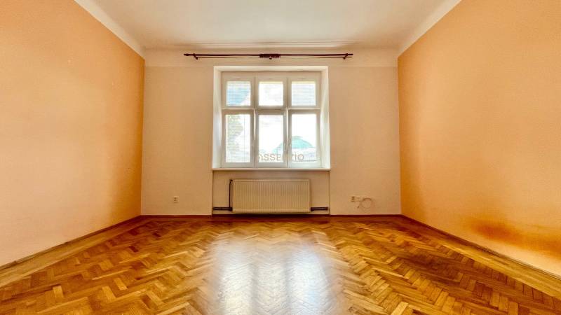 A room with parquet flooring and a large window illuminates the interior of a 2-room apartment.