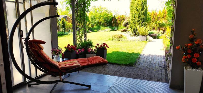 A terrace of a family house with a swing and a view of a garden with greenery.