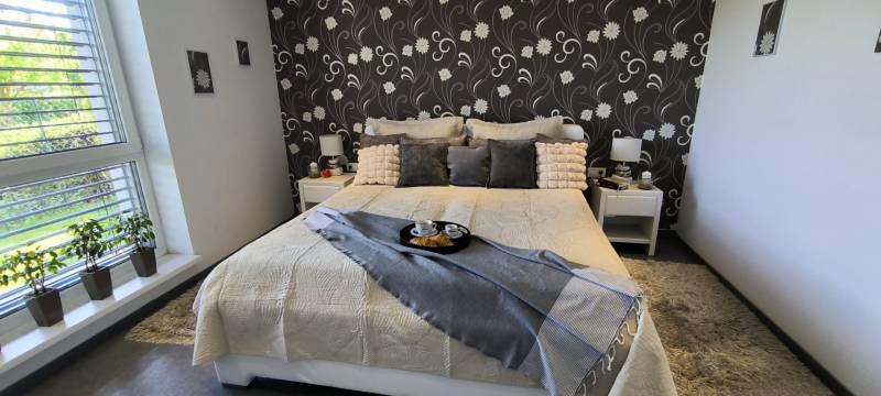 A bedroom in a family house with floral wallpaper and a bed decorated with pillows.