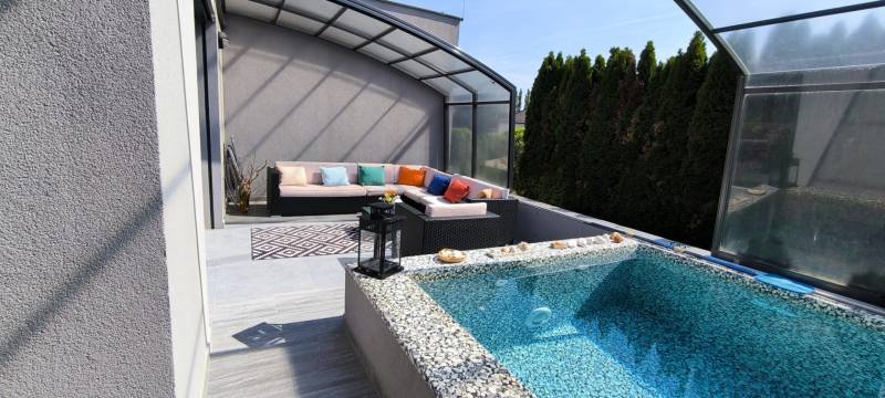 The terrace of a family house in Zurndorf with a swimming pool and seating under a shelter.