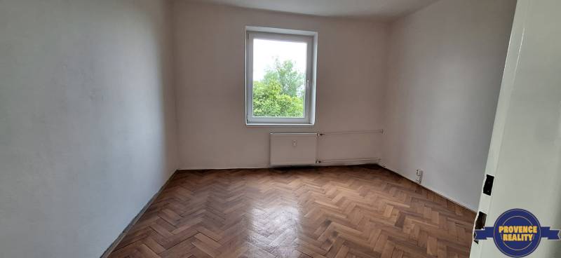 An empty room in a 3-room apartment with a parquet floor and a window overlooking greenery.