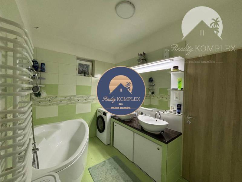 A bathroom in a family house with a bathtub, sink, and washing machine in green and white shades.