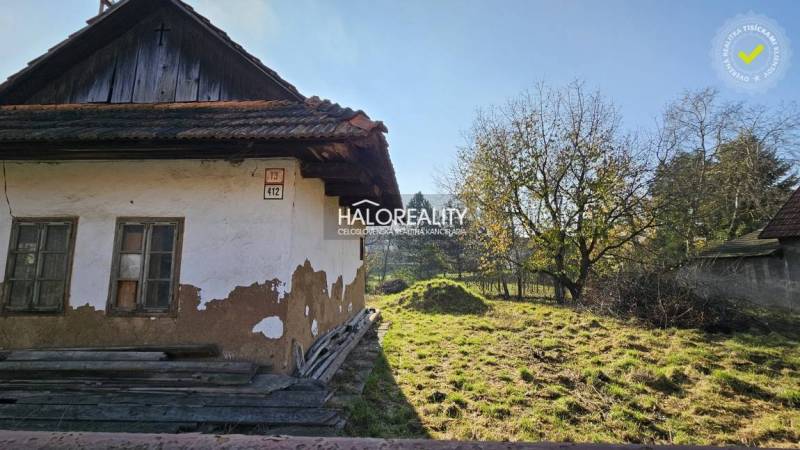 An old house with a damaged facade next to a grassy plot surrounded by trees, perfect for living.