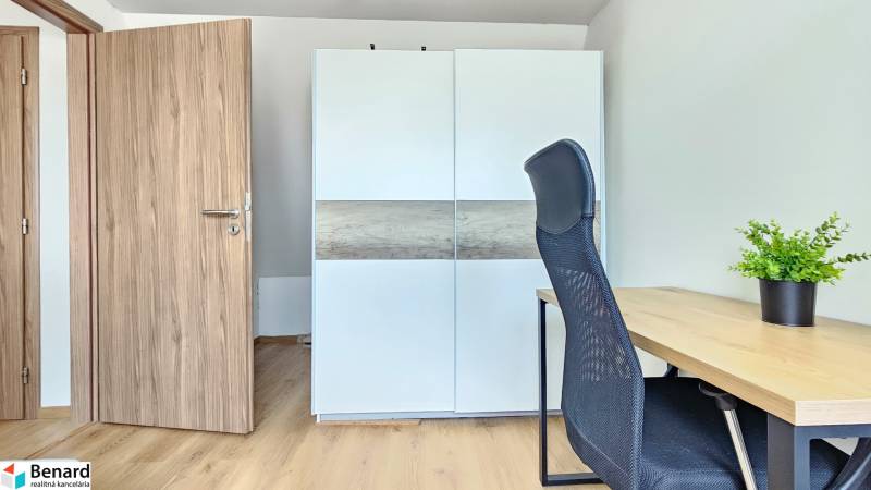 A room with a table, a black chair, a white wardrobe, and a plant in a four-room apartment.