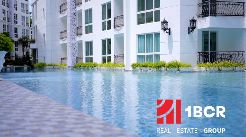 Apartment construction in Pattaya with landscape architecture and a pool in the background of the buildings.