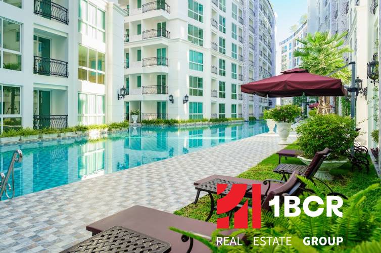 Pattaya, construction of apartments with a swimming pool, deck chairs, and umbrellas in a residential area.