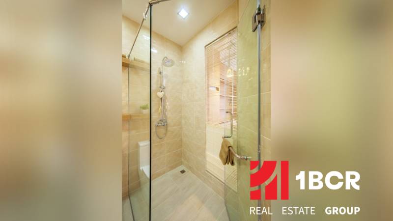 Bathroom in a 2-room apartment with a glass shower enclosure and light-colored tiles.