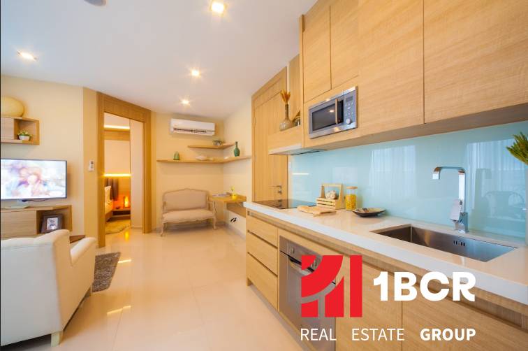 A kitchen in a 3-room apartment with wooden cabinets, a television, and a view of the living room.