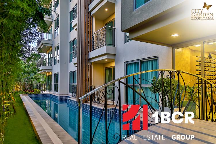 A swimming pool and the facade of a residential building in Pattaya surrounded by greenery.