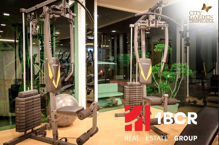 Fitness equipment in apartment construction, green elements, lighting, and mirrored walls.