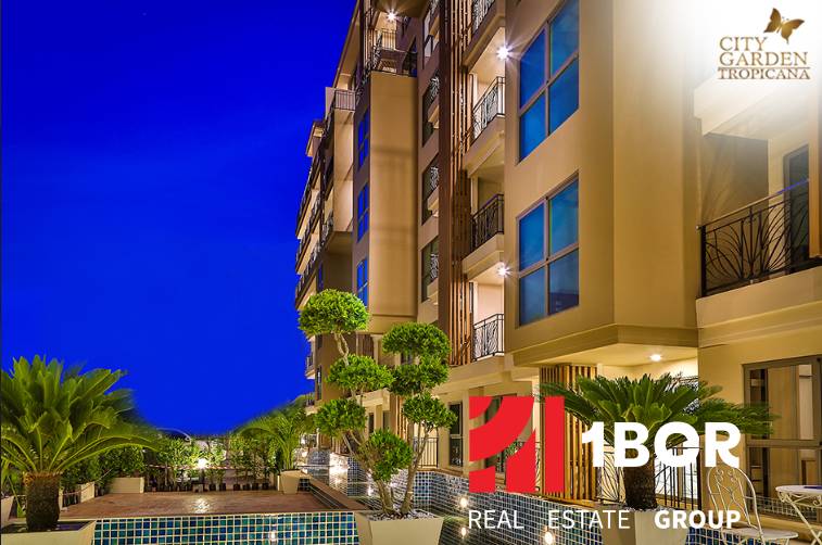 Nighttime construction of apartments in Pattaya with illuminated balconies and green surrounding landscaping.