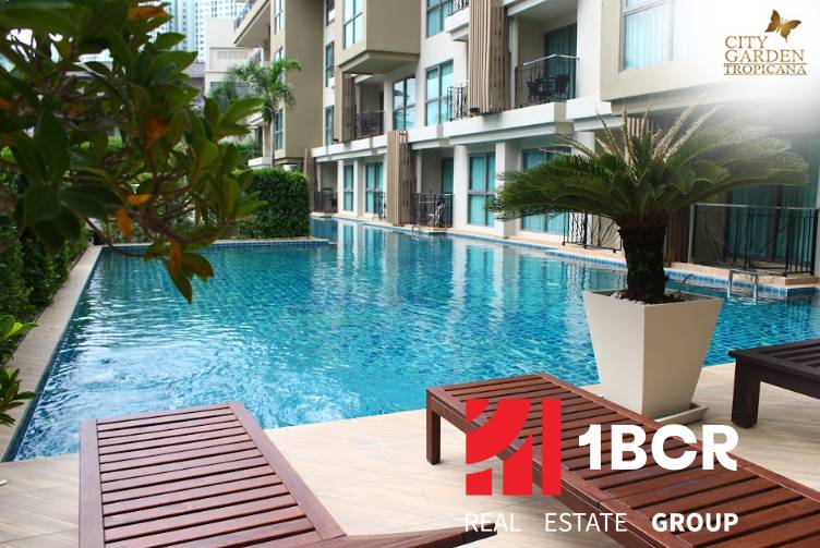A swimming pool during the construction of apartments in Pattaya, surrounded by greenery and loungers.