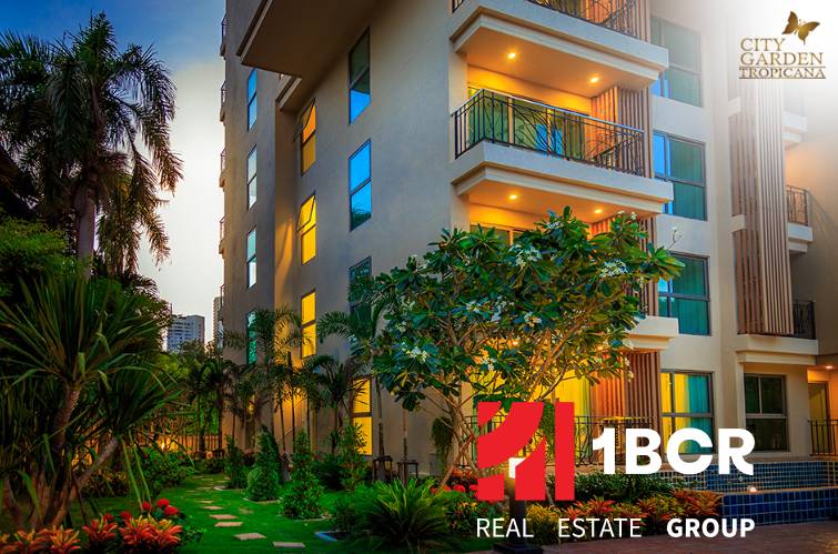 Construction of apartments in Pattaya with a tropical garden and bright balconies in the evening light.