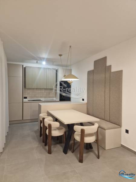 Dining room in a holiday apartment with a kitchen, light chairs, and gray panels on the wall.