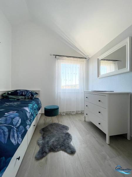 A bedroom in a holiday apartment with a bed, white dresser, and chair on a wooden floor.