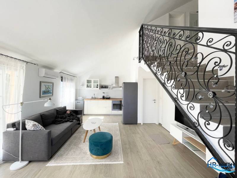 Living area in a holiday apartment with a kitchen, sofa, and staircase.