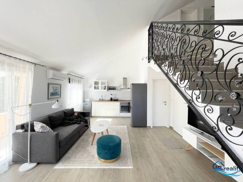 Living room with a sofa, kitchenette, and decorative railing in a holiday apartment.