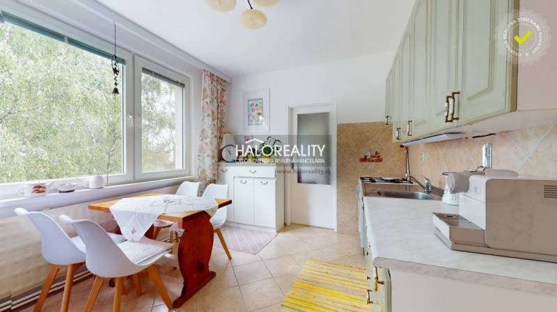 A kitchen in a 4-room apartment with a wooden table, chairs, and a large window with a curtain.