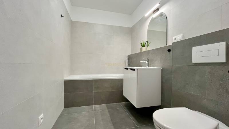 Bathroom with a bathtub, sink, mirror, and toilet in a 2-room apartment.