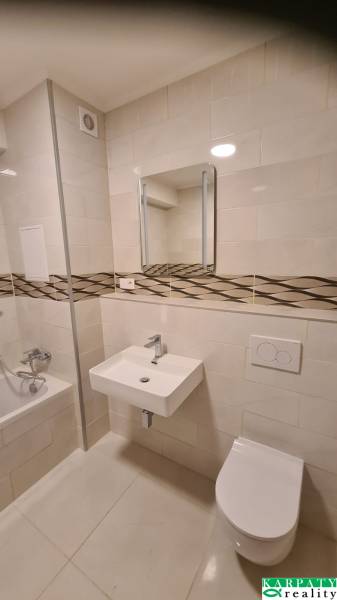 Bathroom in a studio apartment with a bathtub, sink, and toilet, tiles with a decorative strip.