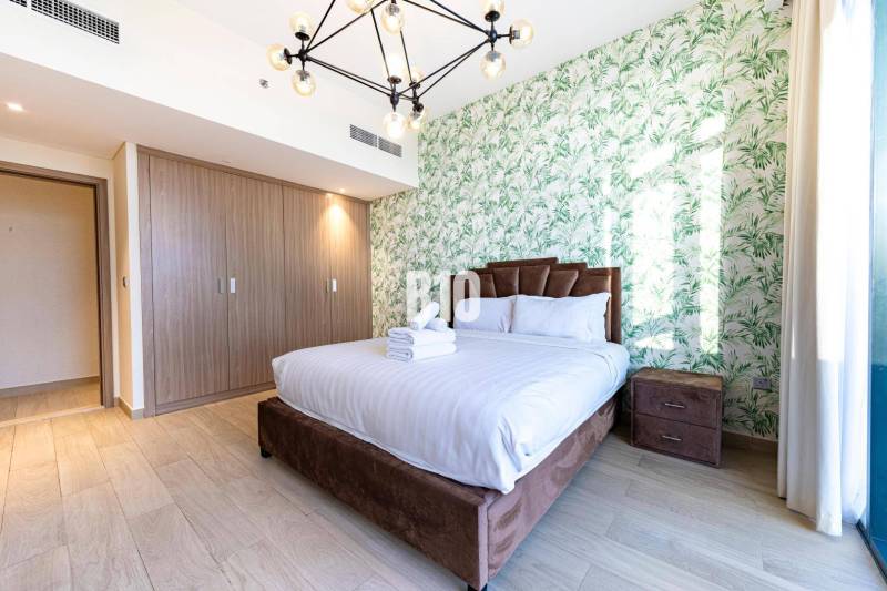 Beautiful bedroom in a 3-room apartment with a bed, botanical wallpaper, and a wooden wardrobe.