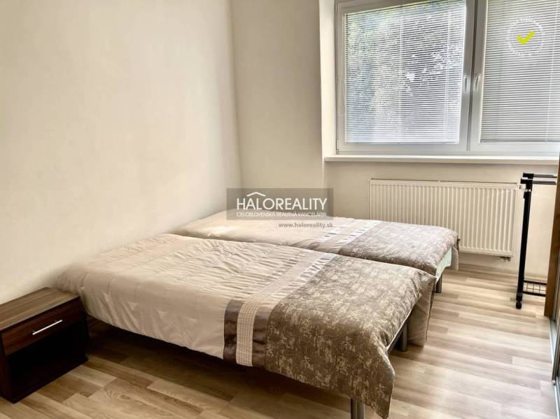 A bedroom in a three-room apartment with two beds, a nightstand, and a large window.