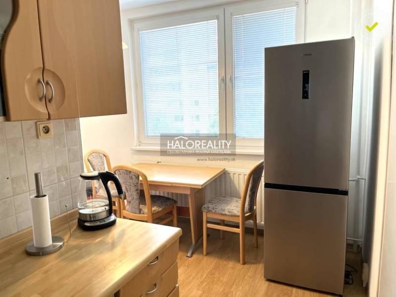 A kitchen in a 3-room apartment with a refrigerator, a wooden table, and chairs.